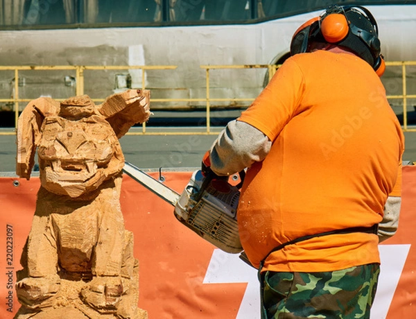 Fototapeta Experienced carpenter making a big wooden dog sculpture with a chainsaw