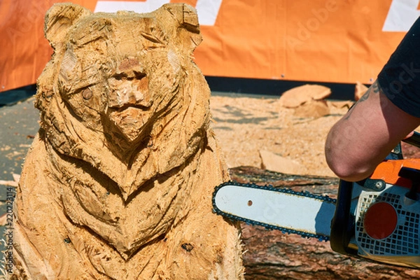 Fototapeta Experienced carpenter making a big wooden bear sculpture with a chainsaw