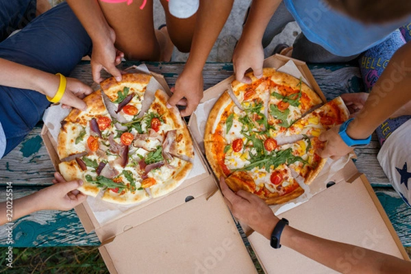Obraz Widok z góry przedstawiający dzieci chwytające kawałki pizzy z pudełka na pikniku na świeżym powietrzu. Ręce dzieci przy pizzy
