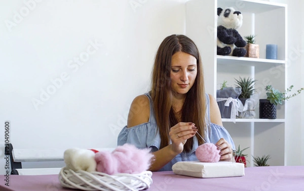 Fototapeta young caucasian woman making wool dry felting tutorial. female showing needle felted toy master class. Hobbies, handmade, crafting, leisure, teaching, education, creativity, design concept