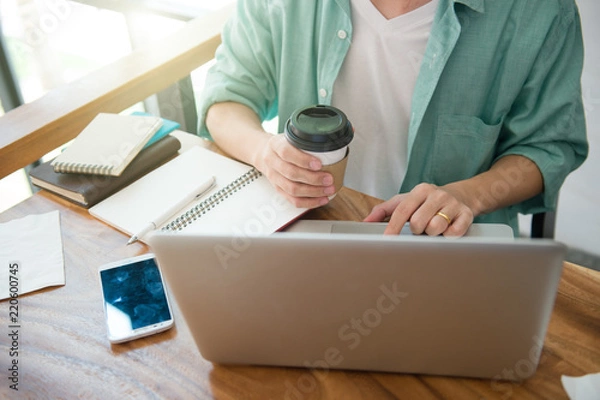 Fototapeta Business male hands typing on a laptop keyboard on desk with a cup of coffee in evening light,Urgent agenda,Freelance work at home office.