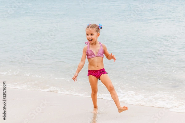 Fototapeta Little beautiful girl dressed in swimsuit stands on the seashore
