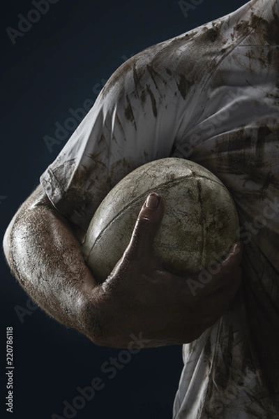 Obraz Rugby player hands with ball on dark background. Close up