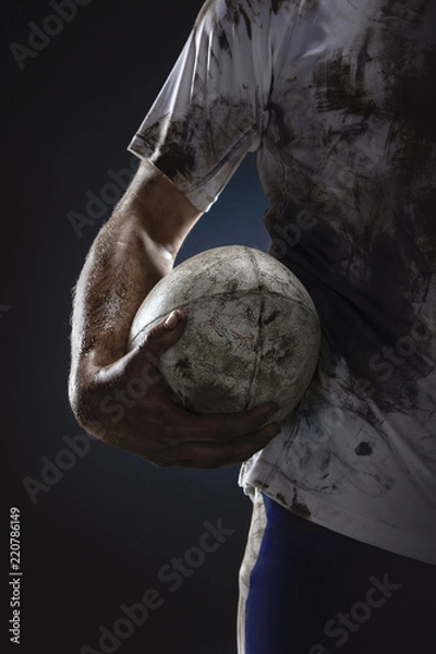 Obraz Rugby player hands with ball on dark background. Close up
