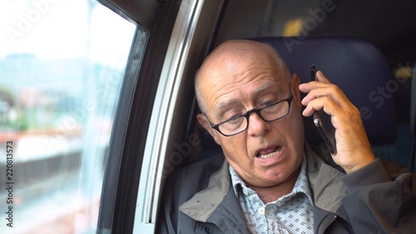 Fototapeta Elderly bald man talking on mobile phone inside moving train - Model Released