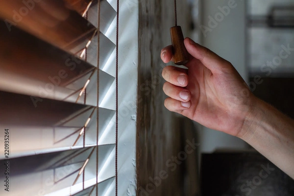 Fototapeta The man's right hand holds one of the control strings of the wooden shutters on the window.