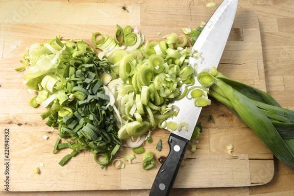 Fototapeta sliced leek and a large kitchen knife on a wooden board, cooking concept, high angle view from above