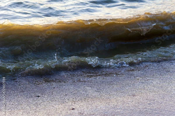 Fototapeta Waves on the sandy shore of a large river. The rays of light are reflected in the waves.