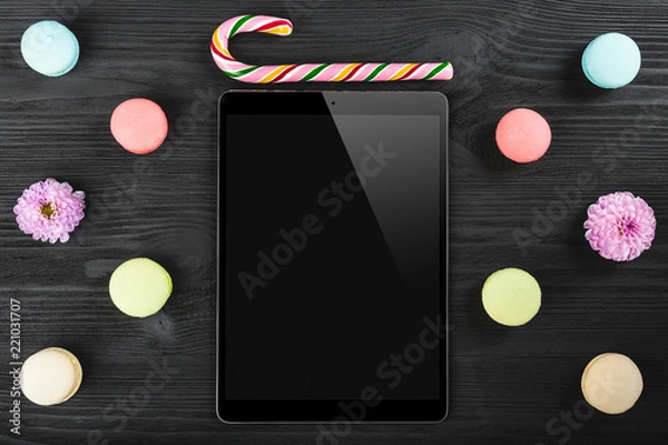 Fototapeta Office desk with macarons, lollipop, tablet-touch screen device and pink plants on black table background. Top view. Flat lay