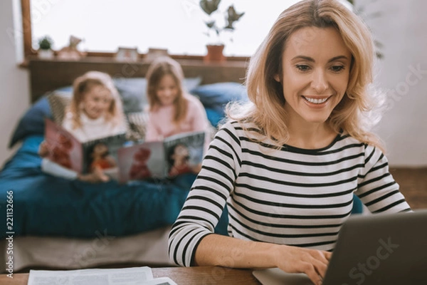 Fototapeta Professional freelancer. Smart cheerful woman using her laptop while working from home