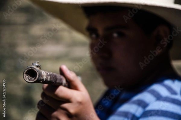 Obraz Close up face of boy with hat pointing with a rifle