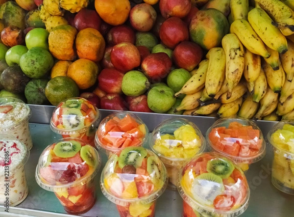 Fototapeta Tropical fruit sales stand. Apples, pears, bananas, tangerines and pitahayas. Fruit salad in plastic bottles with kiwi, papaya and pineapple. Delicious, nutritious and juicy.