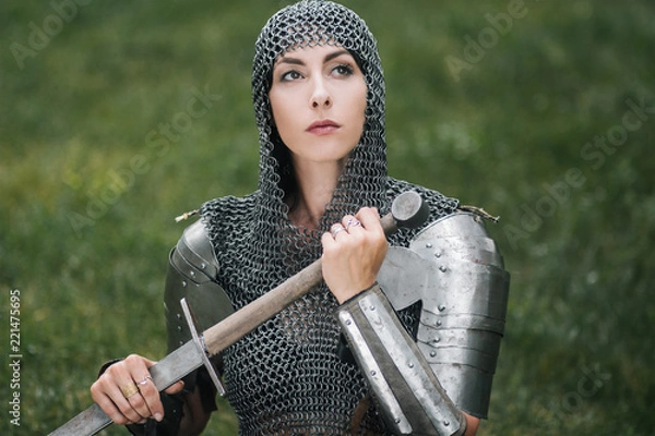 Fototapeta Medieval girl warrior, in a chain mail hood with a sword in his hand. A woman in European armor. Viking. Fantasy