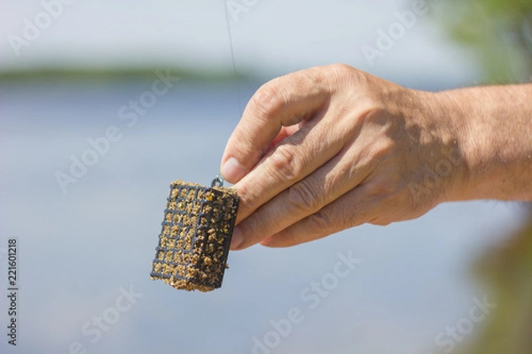 Fototapeta the fisherman holds in his hand a feeder with feeding fish
