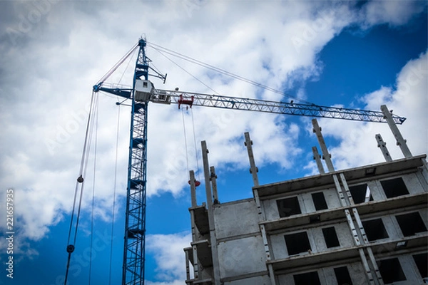 Obraz Construction crane in front of a building against a sky with clouds