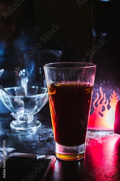 Fototapeta a glass of whiskey, or rum, or alcohol stands on a table on a dark background in the bar