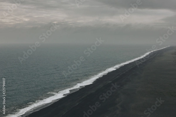 Fototapeta aerial view of coastline with black sand beach near wavy ocean under cloudy sky in Vik, Iceland