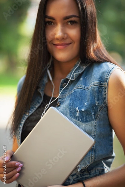 Fototapeta Young pretty brunette girl with the tablet and listening to music on the street in summer.