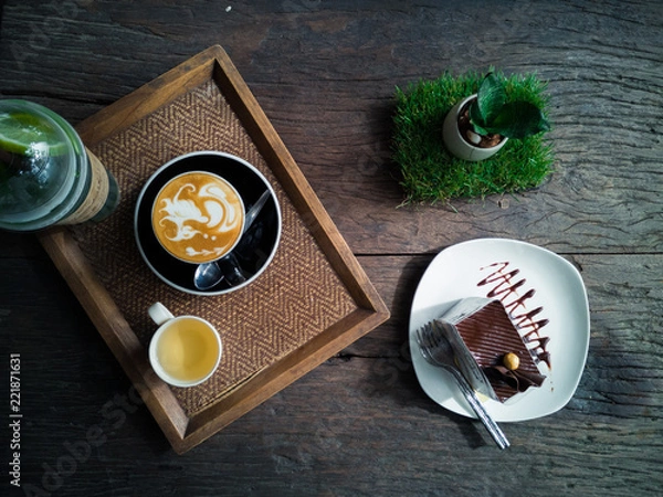 Obraz Top view of a cup of coffee with cup of tea and chocolate cake on wooden plate.