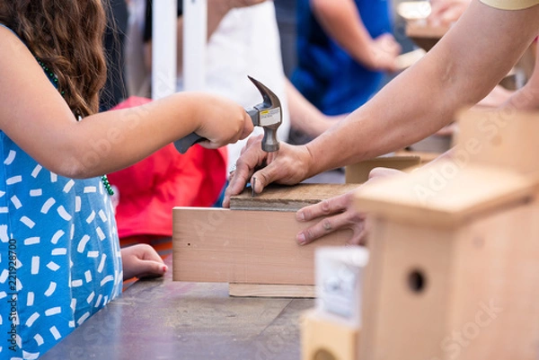Fototapeta Young girl child with a hammer building bird treehouse with a help of an adult.