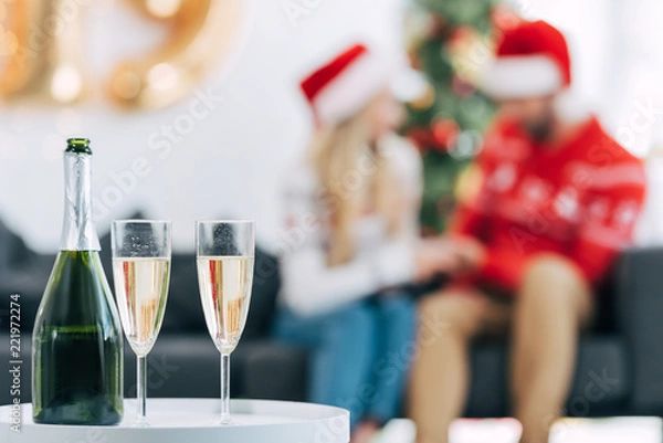 Obraz selective focus of champagne bottle and glasses for celebrating christmas, couple sitting behind