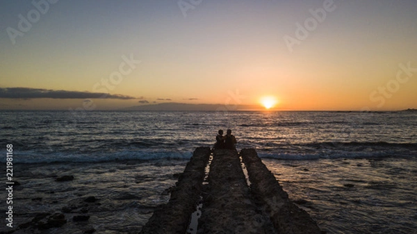 Fototapeta romantic aged senior couple sitting together at the end of the dock looking the sunset and enjoying love and relationship foreverness. life and enjoy the nature concept for two caucasian adults 