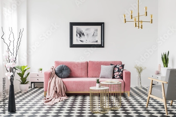 Fototapeta Poster above pink sofa in spacious living room interior with patterned armchair and plants. Real photo