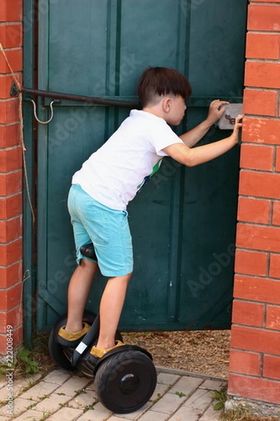 Fototapeta The brunette boy on the gyroscope left to open the door. - Who's come? Life in the village in the summer. Holiday.