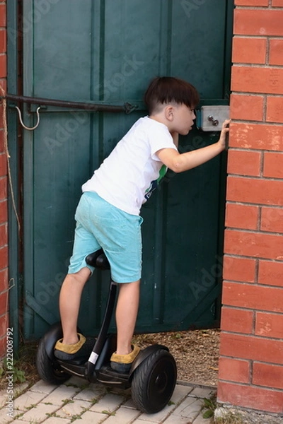 Fototapeta The brunette boy on the gyroscope left to open the door. - Who's come? Life in the village in the summer. Holiday.