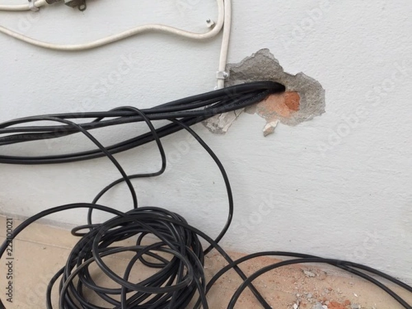 Fototapeta break in the wall with protruding electrical wires, Electric wire sticking out of a white wall, crack hole wall with electric wires