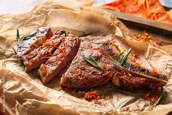 Obraz Parchment with cut grilled steak and spices on wooden board