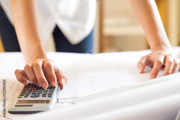 Fototapeta closed up of lady architect put hand on calculator for calculating design in blueprint