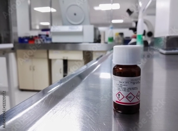 Fototapeta Amber bottle (dark glass) for storage of a chemical substance, in a scientific laboratory. White cap and symbols of attention and danger on the label.