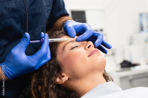 Fototapeta Close up of beautician expert's hands injecting botox in female forehead.