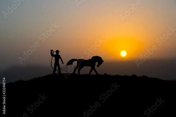 Fototapeta Cowboy concept. Silhouette of Cowboys at sunset time. A cowboy silhouette on a mountain with an yellow sky.