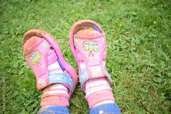 Fototapeta the legs of a little girl in sandals and socks are smeared with sand