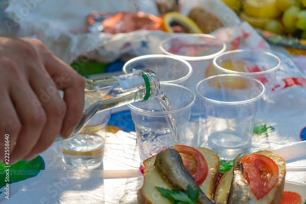 Fototapeta Vodka is poured into plastic glasses. A bottle in a man's hand.