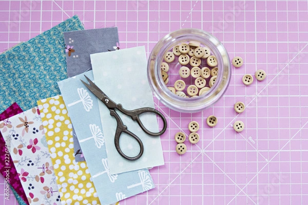 Fototapeta Wooden buttons in jar, retro scissors, cotton fabric scraps and pink cutting mat