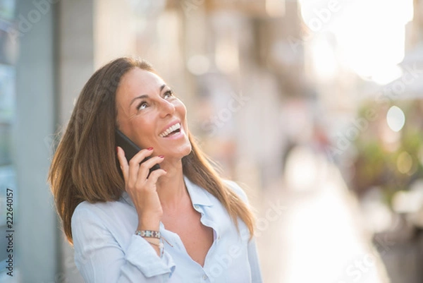 Fototapeta Beautiful middle age hispanic woman standing talking on the phone with smile on face at the street. Walking through the smiling confident and cheerful on a sunny day.
