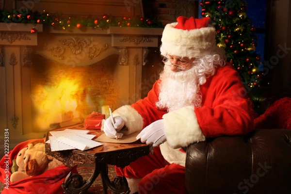 Obraz Portrait of happy Santa Claus sitting at his room at home near Christmas tree and answering Christmas letters.