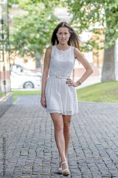 Fototapeta Beautiful young girl in a white summer dress near a showcase with reflection
