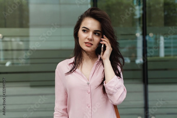 Fototapeta Busy female manager calling with cell telephone outside, woman talking via mobile phone and walking on the city street, manager working remotely and making phone call via modern smartphone outdoors