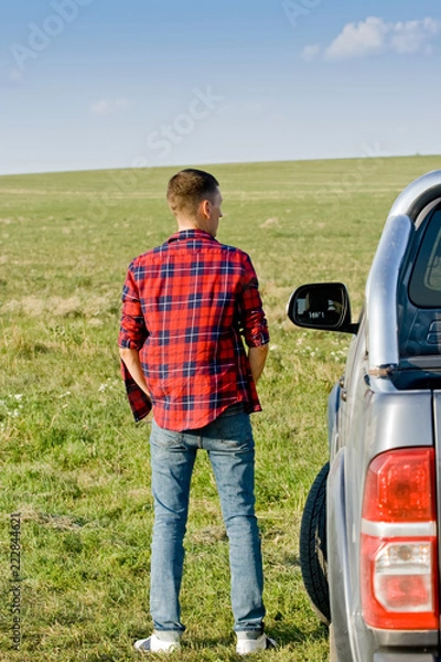 Obraz Young man in checkered shirt stand near the car on the green field