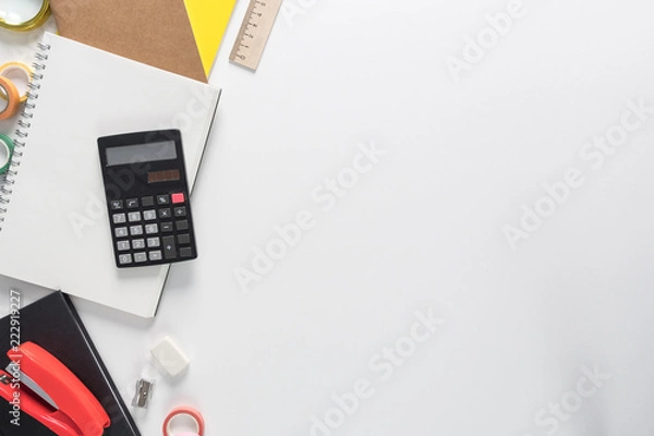 Fototapeta Top view over a school supplies as calculator, rulers, tapes, paper clips, notebooks and other stuff from left side of a a white background. Back to school concept. Office supplies flat lay