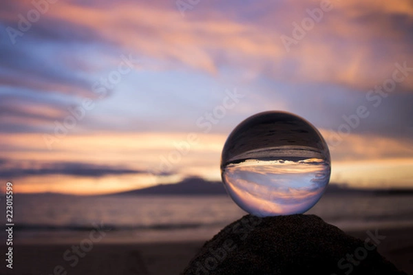 Fototapeta Pink Clouds at Sunset over Ocean with Island Captured in Glass Ball