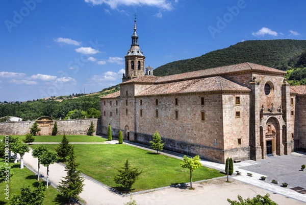 Fototapeta Spain, La Rioja, San Millan de la Cogolla: Panoramic view of famous Monastery of San Millan de Yuso with public park, hills and blue sky. It's the birthplace of modern written spoken Spanish language.