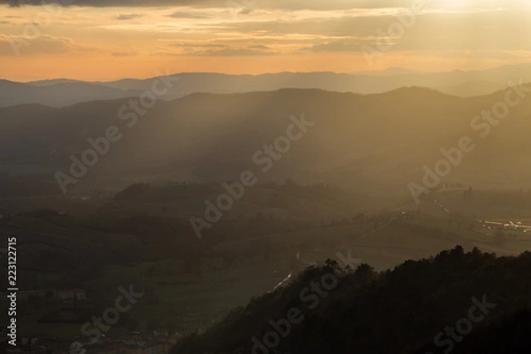 Fototapeta Sunrays coming over a valley in Umbria (Italy) with some plants in the foreground