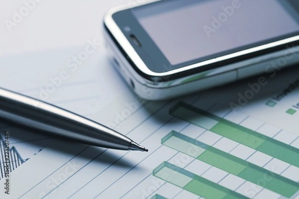 Fototapeta Mobile Phone And Pen On Financial Graphs Close-up