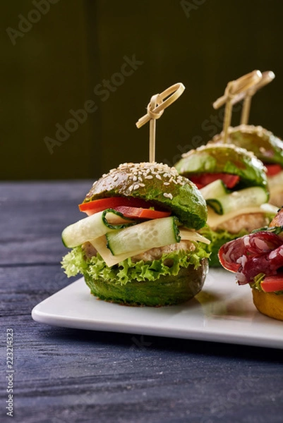 Fototapeta Fashionable set of multi-colored small hamburgers. Snack in the form of sandwiches with different fillings on a square plate. A treat for a buffet. Vegetarian and meat burgers.
