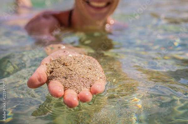 Fototapeta A woman holds sand from the bottom of the sea in her hand. Wet sand from the seabed in the hand